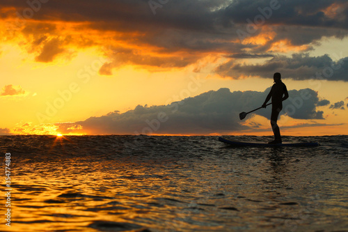 Stand Up Paddle Boarding In Japan at Sunrise and Sunset a solo rider keeping fit & healthy on the Pacific Ocean in a black wetsuit, also catching some large waves, The ocean is blue with a nice sky. © Dane