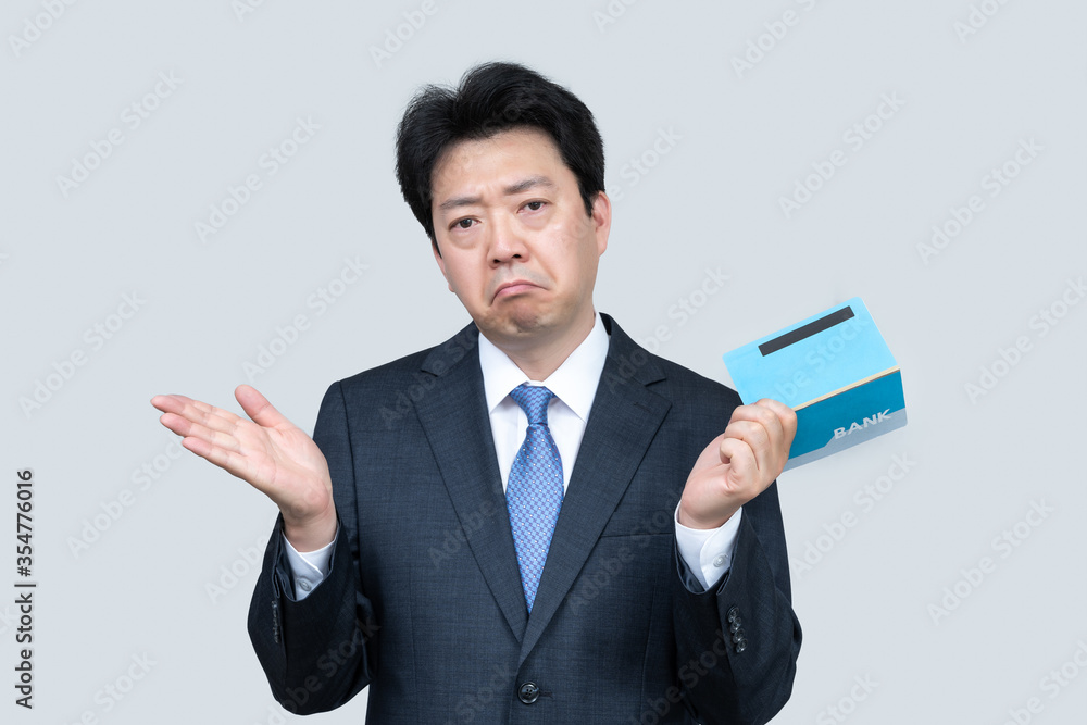 A middle-aged Asian businessman holding a bank passbook in his hand on a gray background. A middle-aged Asian businessman holding a bank passbook in his hand on a gray background.