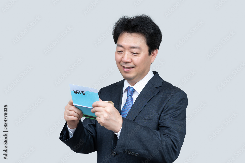 A middle-aged Asian businessman holding a bank passbook in his hand on a gray background. A middle-aged Asian businessman holding a bank passbook in his hand on a gray background.