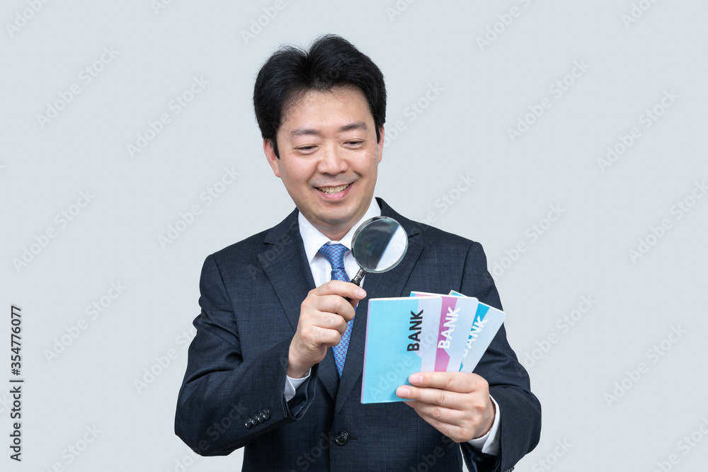 A middle-aged Asian businessman holding a bank passbook in his hand on a gray background. A middle-aged Asian businessman holding a bank passbook in his hand on a gray background.