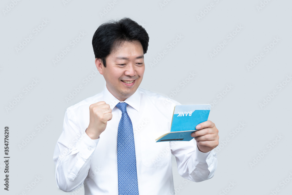 A middle-aged Asian businessman holding a bank passbook in his hand on a gray background.