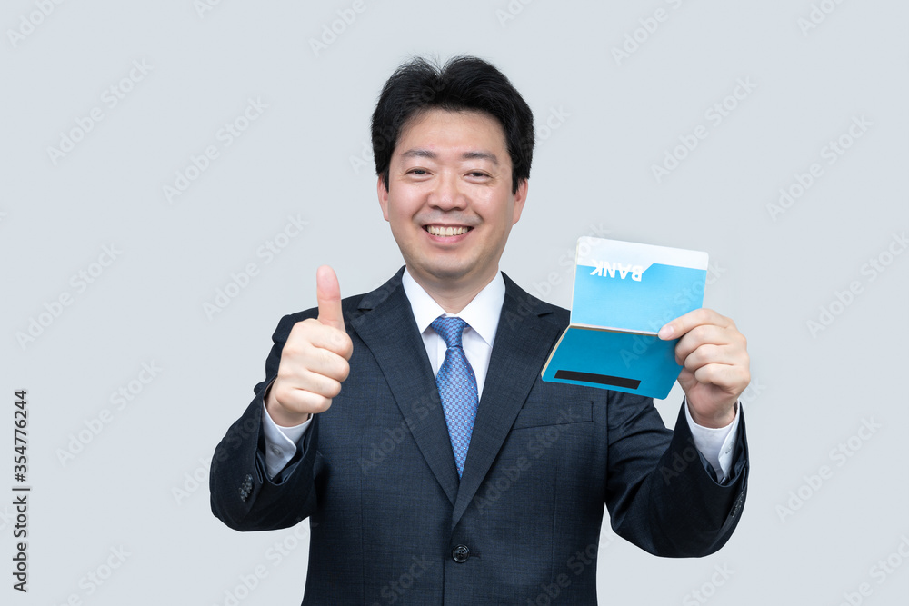 A middle-aged Asian businessman holding a bank passbook in his hand on a gray background. A middle-aged Asian businessman holding a bank passbook in his hand on a gray background.
