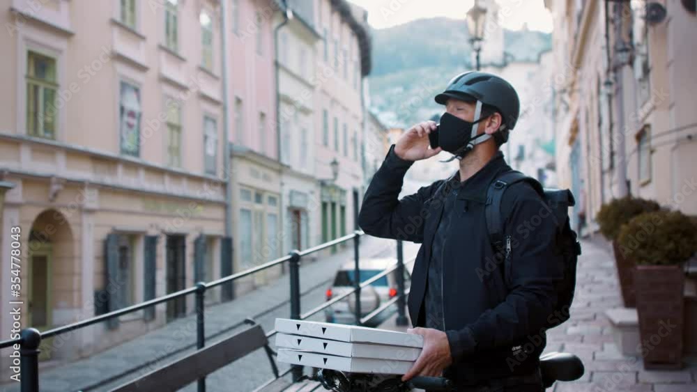 Delivery man courier with face mask and smartphone delivering pizza in town. Delivery man courier with face mask and smartphone delivering pizza in town.
