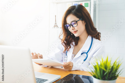 Medical health clinic beautiful Asian doctor working using smart tablet touching, stethoscope diagnosing patient analysis research examination healthcare provider service insurance in modern office