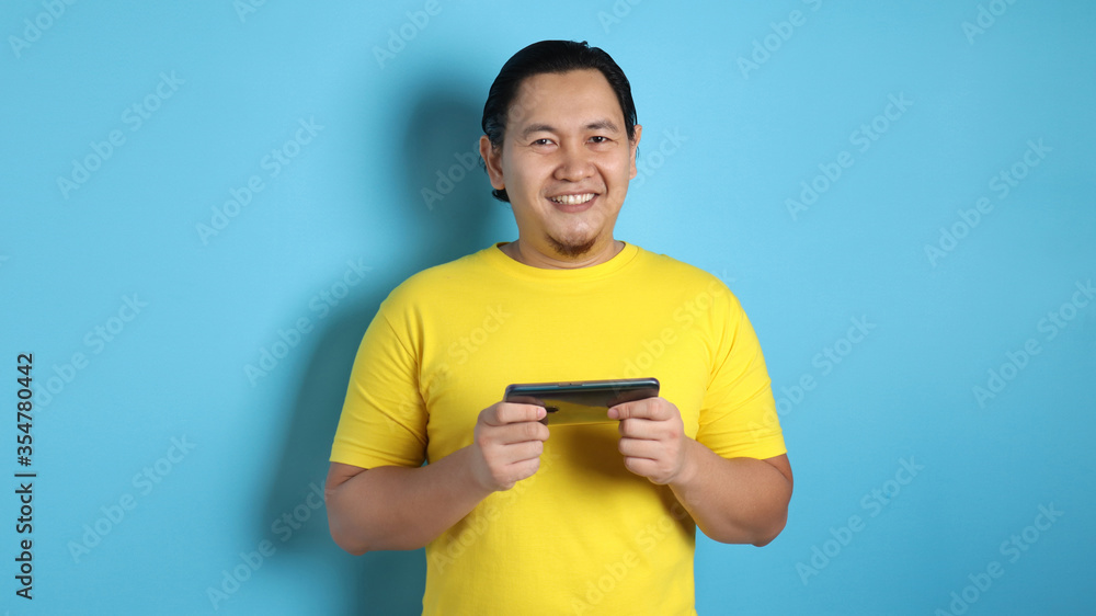 Funny Young Asian Guy Playing Games on Tablet Smart Phone Funny Young Asian Guy Playing Games on Tablet Smart Phone
