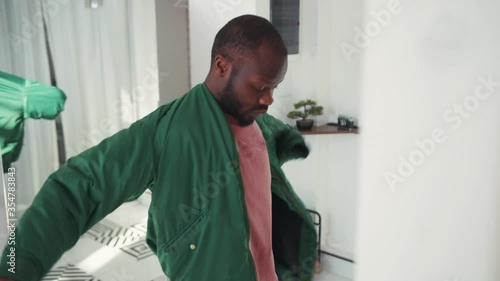 Black handsome guy getting dressed for work in front of mirror. Young african man wearing jacket and leaving house with laptop for work. Going out. Lifestyle.