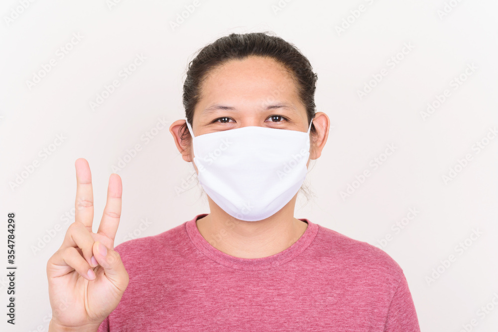Portrait of Asian man wearing white fabric mask to protection corona virus outbreak and showing v sign Portrait of Asian man wearing white fabric mask to protection corona virus outbreak and showing v sign