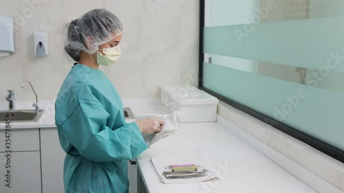 Woman doctor assistant in white gloves and green gown is wiping odontic instruments after washing, before sterilization and puts on the tablecloth in the dental office. photo