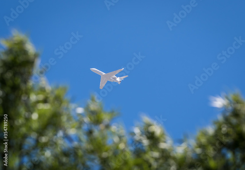 White Jet flying over trees against blue sky in Sonoma County Ca, USA.