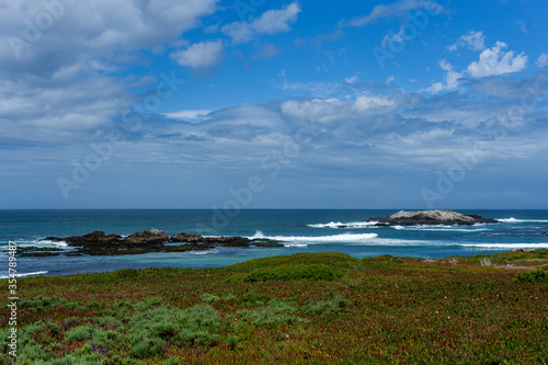 Rocky blue Pacific ocean coastal landscape with waves breaking against the rocks under a dramatic partly cloudy sky