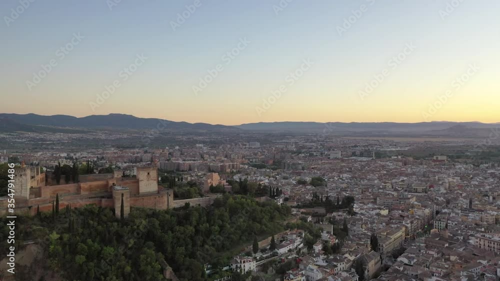 Aerial panning shot of famous palace on hill against sky during sunset, drone flying over houses in city - Granada, Spain Aerial panning shot of famous palace on hill against sky during sunset, drone flying over houses in city - Granada, Spain