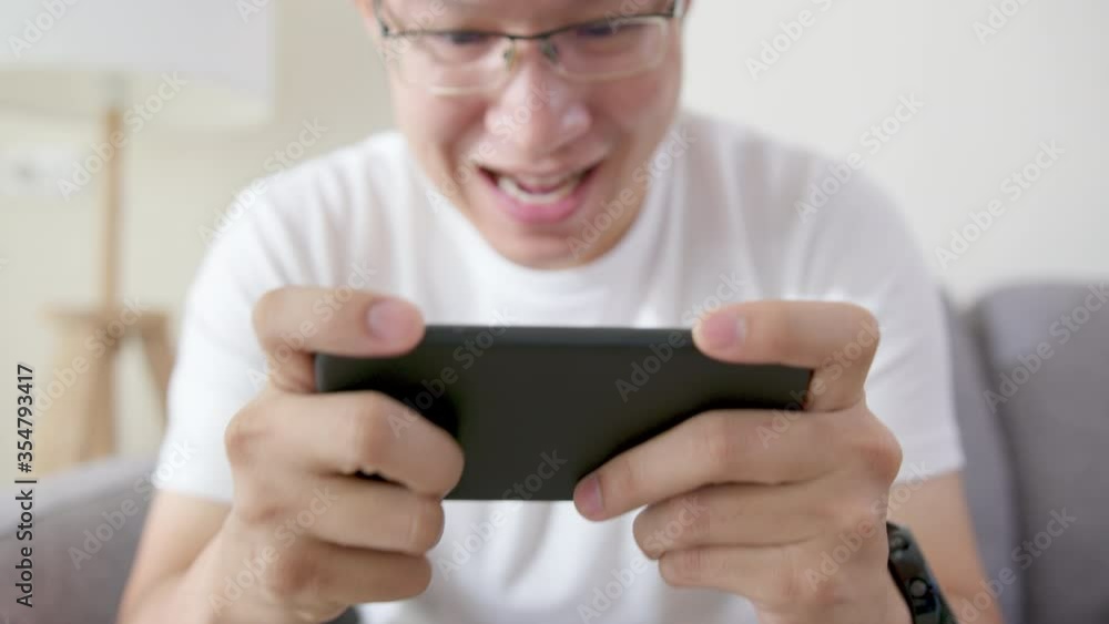 Close up asian man's hand playing online game via smartphone digital gadget at living room. Happy male feeling funny and excite with win competition game e-sport entertainment network. Close up asian man's hand playing online game via smartphone digital gadget at living room. Happy male feeling funny and excite with win competition game e-sport entertainment network.