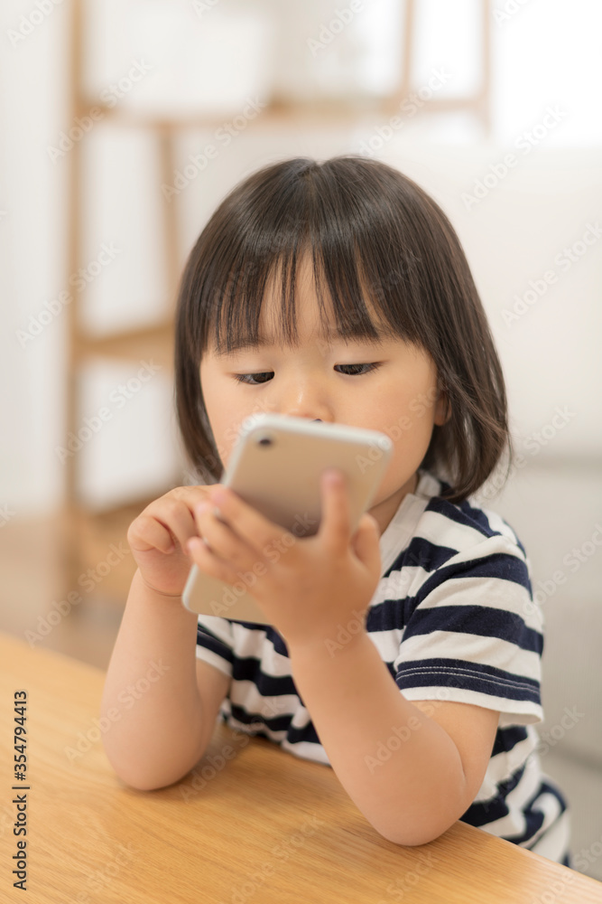 自宅の居間でスマートフォンを見る3歳の女の子