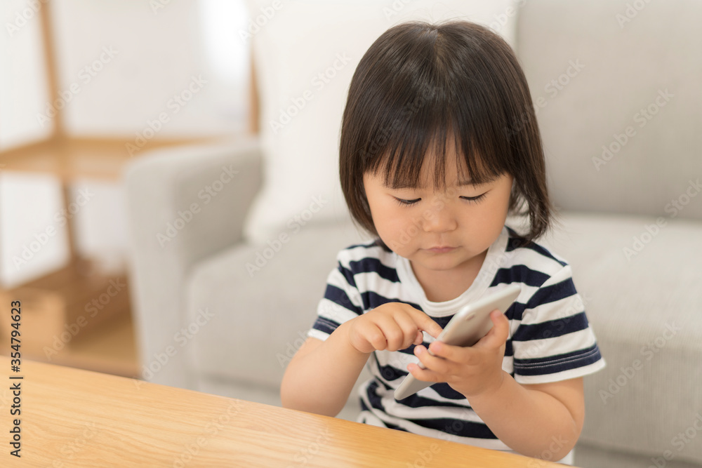 Naklejka premium 自宅の居間でスマートフォンを見る3歳の女の子