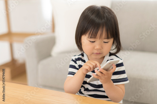 自宅の居間でスマートフォンを見る3歳の女の子
