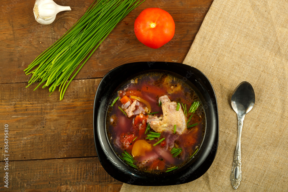 A black dish of vegetable soup with vegetables on a table in the background. A black dish of vegetable soup with vegetables on a table in the background.