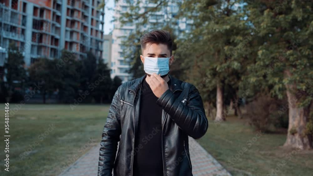 Young man dressed in a black jacket sitting outdoors and wearing a medical mask to protect others from the spread of the virus. . 4k Young man dressed in a black jacket sitting outdoors and wearing a medical mask to protect others from the spread of the virus. . 4k