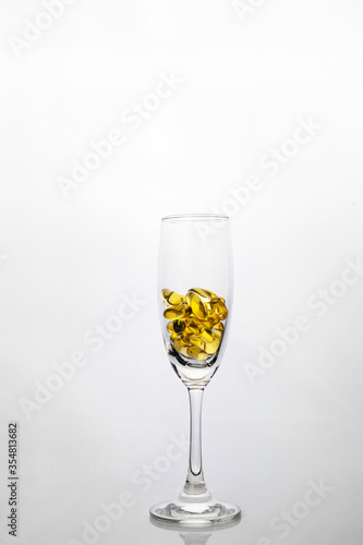 yellow fish oil vitamin supplementary pill in champagne drinking glass in healthy well-being lifestyle concept on white background