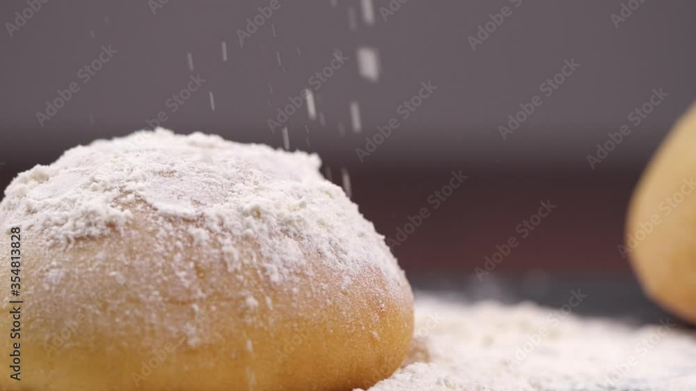 Flour falling on bread in a bakery in slow motion. Cook sifts the flour for the dough. Sprinkling flour over bun on kitchen table. Shot with slide or move camera Flour falling on bread in a bakery in slow motion. Cook sifts the flour for the dough. Sprinkling flour over bun on kitchen table. Shot with slide or move camera