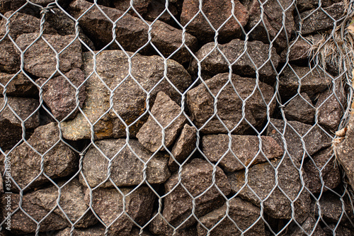 Stack of rocks piled up on top of each other held back by a chicken wire fence. Close up shot of stone wall formed by pile of rocks 