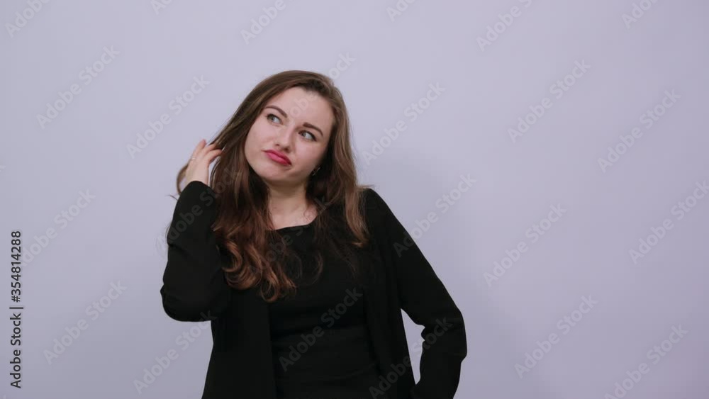 Young attractive woman brunette in a black t-shirt and sweater on white background female touching her hair, discontented, angry human Young attractive woman brunette in a black t-shirt and sweater on white background female touching her hair, discontented, angry human