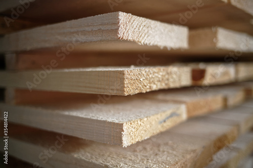 Stack of natural rough wooden boards close-up. Storage of wood in a carpenter's workshop or at a sawmill