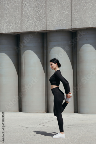 A distant shot of a girl practicing outdoors and stretching quadriceps on the outside of her thigh photo