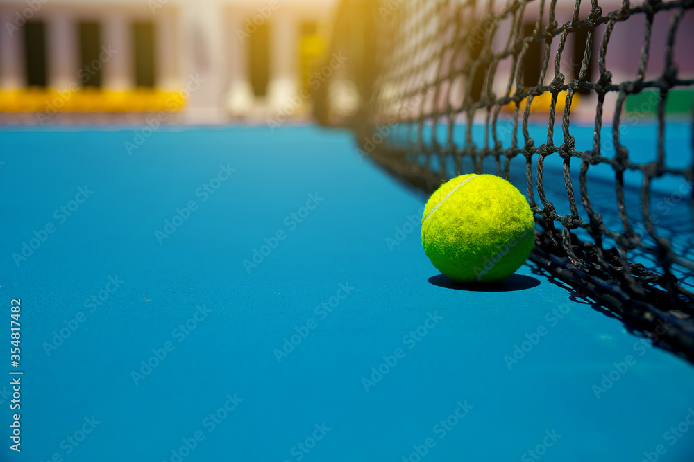 The yellow tennis ball on the blue hard court and the outdoor black net

S