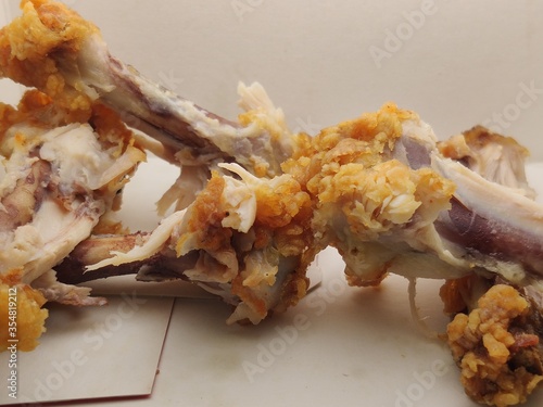 Close-up of chicken bones in a white paper plate, food waste.