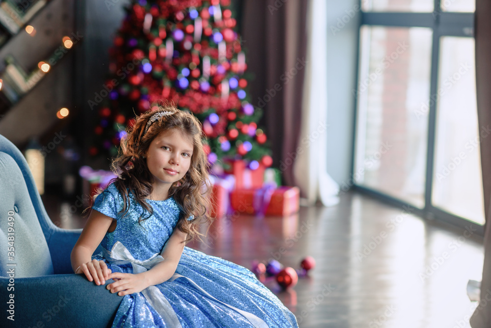 girl with dark hair standing on a box with gifts. Christmas tree in the background. smiles girl with dark hair standing on a box with gifts. Christmas tree in the background. smiles