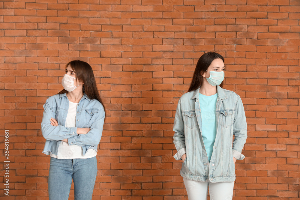 Young women near brick wall. Concept of social distance during coronavirus epidemic Young women near brick wall. Concept of social distance during coronavirus epidemic