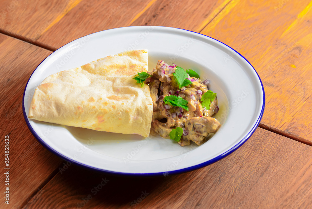 Meat with gravy and fresh greenery served with a piece of lavahs bread on white plate over dark rustic background. Meat with gravy and fresh greenery served with a piece of lavahs bread on white plate over dark rustic background.