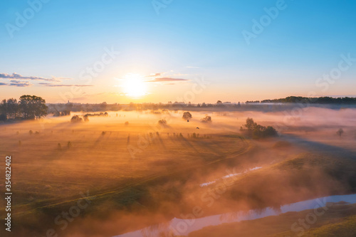 Morning fog in the meadows and at the mouth of the river during sunrise in the countryside  aerial view height of the landscape on the horizon  a forest and a village with flying birds.