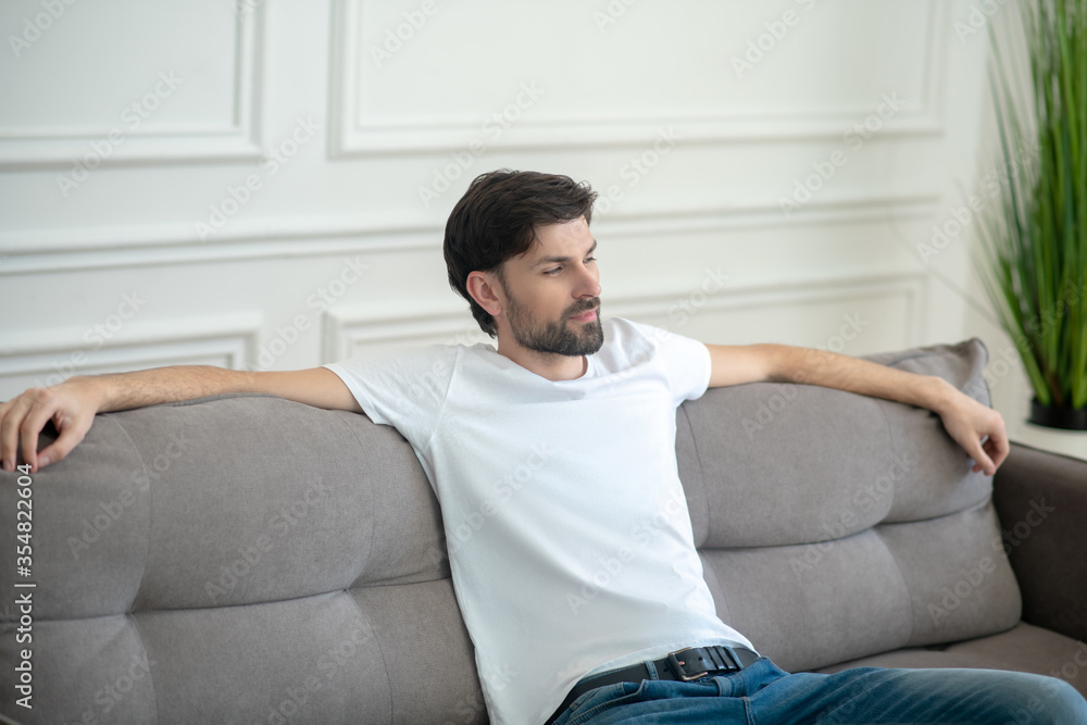 Young bearded man in white tshirt on couch.