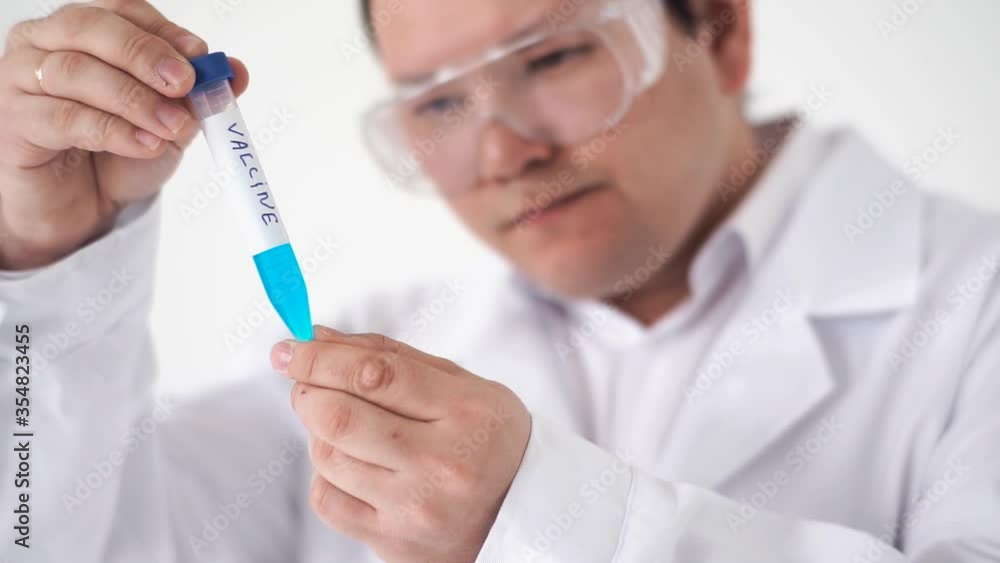 A young concentrated Asian doctor in a white coat, glasses and gloves examines a filling test tube with blue solutions.holding a flask of blue liquid in a chemical research laboratory A young concentrated Asian doctor in a white coat, glasses and gloves examines a filling test tube with blue solutions.holding a flask of blue liquid in a chemical research laboratory