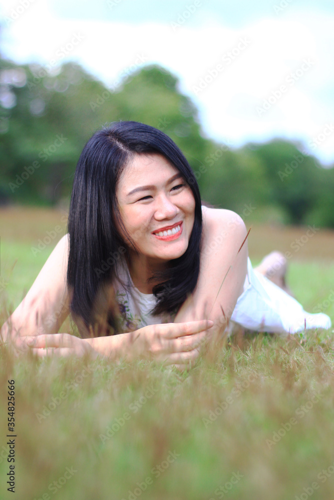 Beautiful asian woman in white dress relax and smiling on green field in natural park. Thai girl enjoy on holiday with sunlight in garden Beautiful asian woman in white dress relax and smiling on green field in natural park. Thai girl enjoy on holiday with sunlight in garden