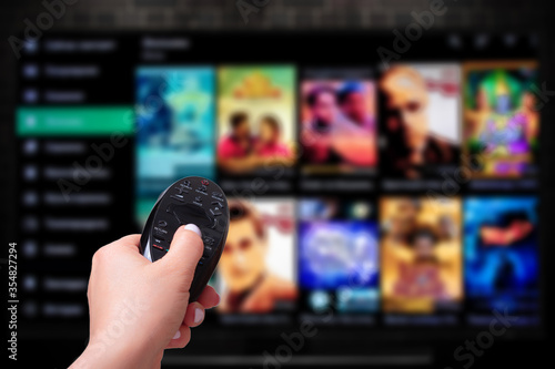 Multimedia streaming concept. Hand holding remote control. TV screen with lot of pictures. photo