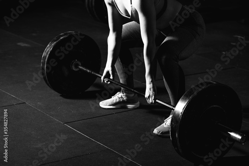 Young strong muscular fit girl with big muscles preparing for hard strength weight lifting or dead lift cross workout training with barbell weights in the gym real people exercising