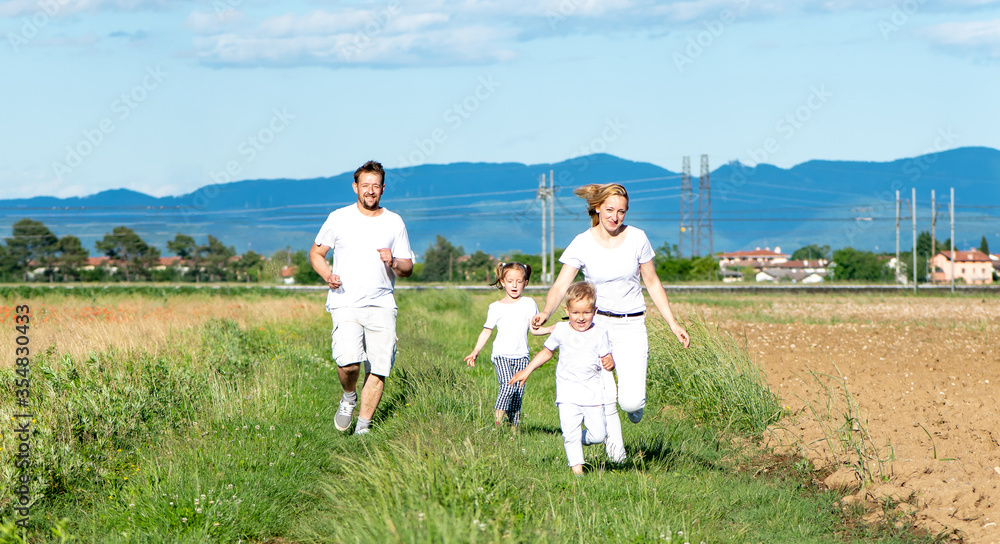 happy family of four runs across the field in white t-shirts
