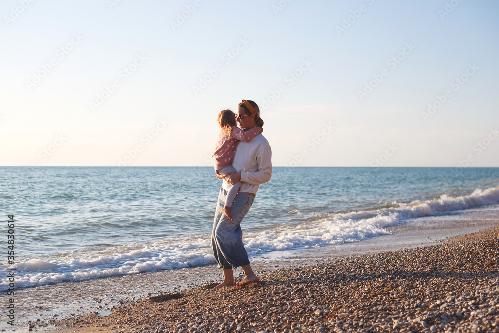 mom and daughter hug and kiss on the beach at sunset