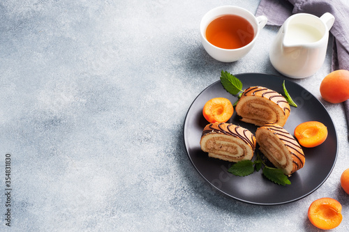 Pieces of sweet roll with cream filling on a plate. Fresh apricot berries and mint leaves.