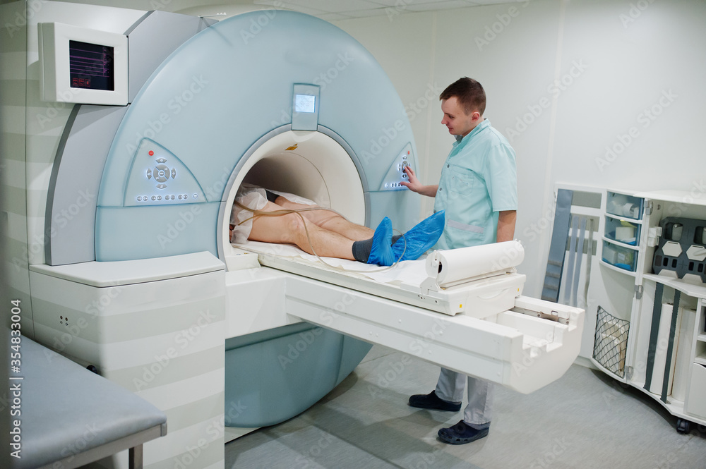 Male doctor turns on magnetic resonance imaging machine with patient inside. Male doctor turns on magnetic resonance imaging machine with patient inside.