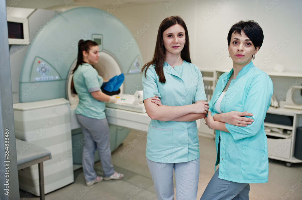 Three female doctors near magnetic resonance imaging machine with patient inside. Three female doctors near magnetic resonance imaging machine with patient inside.