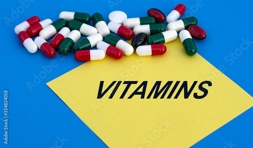 VITAMINS word on yellow paper on a blue background with tablets photo