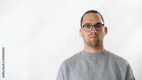 Portrait of serious attractive man in glasses and headphones. Emotional handsome guy is standing and looking at the camera on white background  © markwar