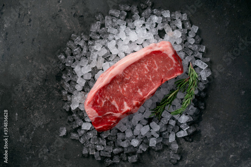 Raw fresh New York beef steak on ice with herbs and rosemary, top view and copy space