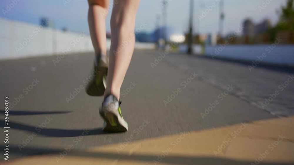 Rear view follow shot of legs of unrecognizable female athlete running down embankment during city marathon Rear view follow shot of legs of unrecognizable female athlete running down embankment during city marathon