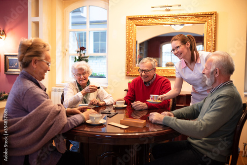 Nurse serving tea while older people play board games