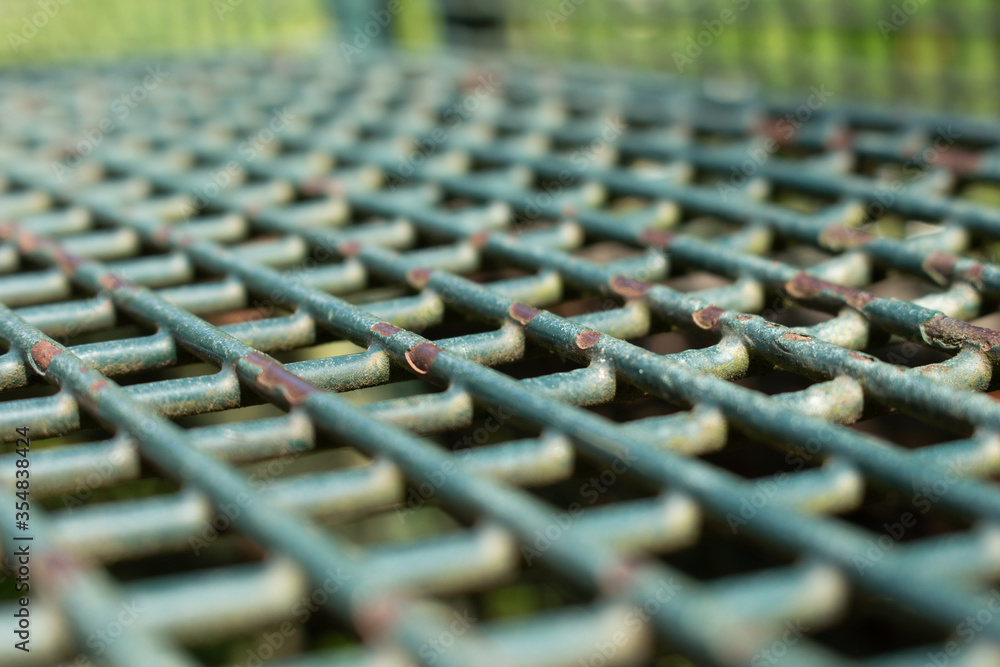 Fototapeta premium Slanted view of a green metal park bench grid with paint peeling off, selected focus