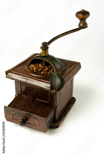 Molinillo de café marrón con granos de café en el interior y café molido en cajón sobre fondo blanco